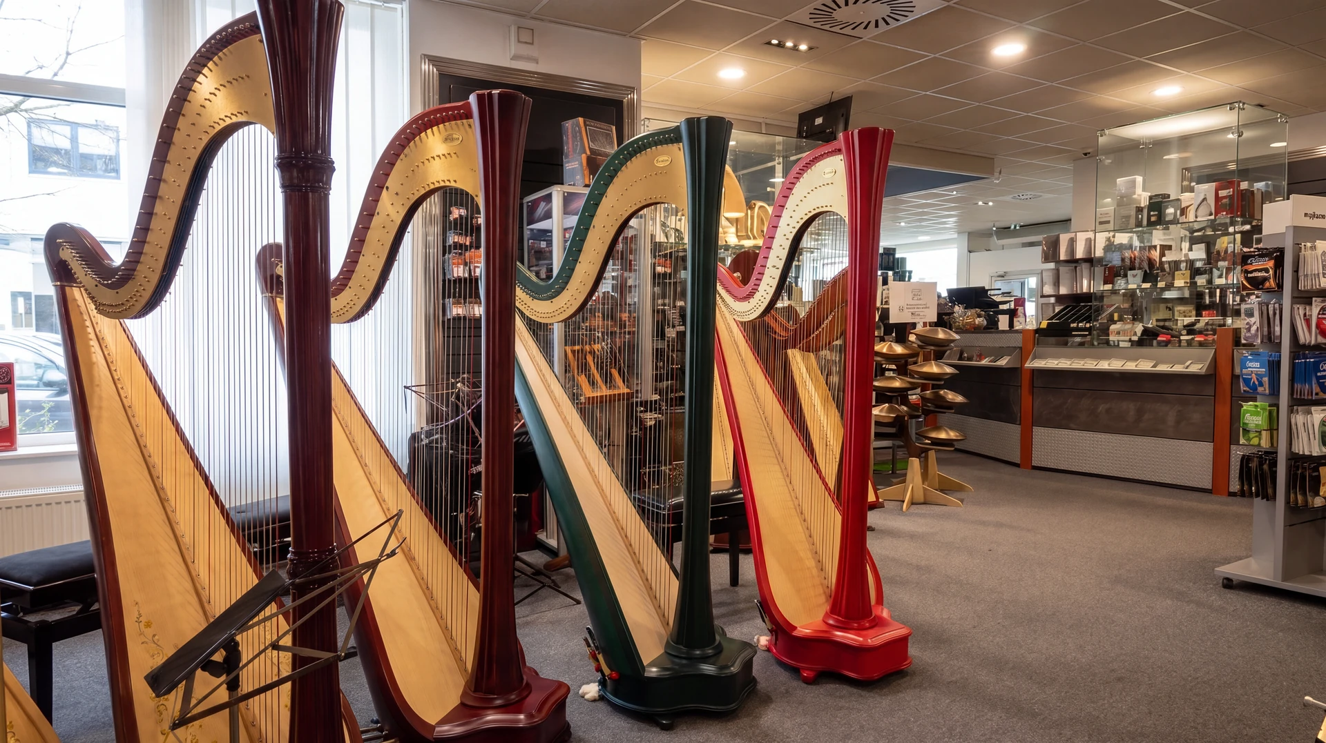 Photo réaliste grand angle de l’intérieur lumineux d’un magasin de musique haut de gamme, avec plusieurs pianos acoustiques et numériques exposés au premier plan, une rangée d’instruments à vent en laiton polis sur présentoirs en arrière-plan, quelques guitares et accessoires visibles sur les côtés, ambiance élégante de showroom professionnel, éclairage naturel et soigné, profondeur de champ légère, sans personne, sans texte ni logo.